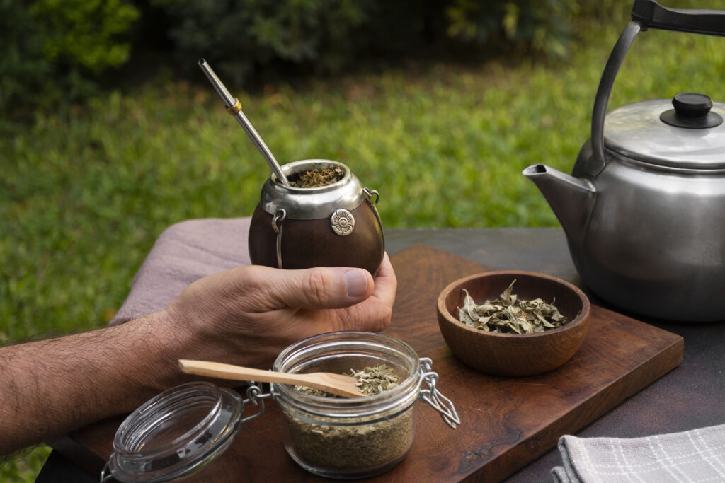 Persona sosteniendo un mate tradicional con bombilla, junto a yerba, pava y utensilios sobre una tabla.